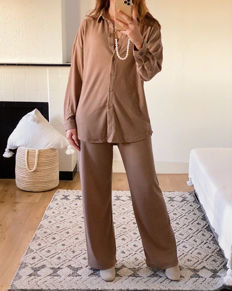 May include: A brown ribbed knit shirt and matching pants set. The shirt has a collared neckline and long sleeves. The pants are wide-legged and have a straight fit.