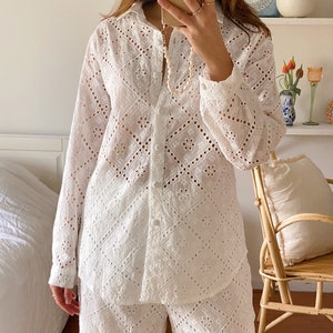 May include: White eyelet pajama set with a button-up shirt and matching pants. The shirt has a collar and long sleeves. The pants have a wide leg.