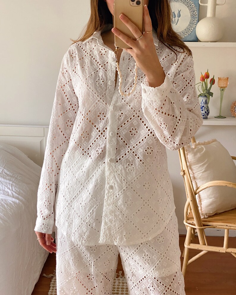 May include: White eyelet pajama set with a button-up shirt and matching pants. The shirt has a collar and long sleeves. The pants have a wide leg.