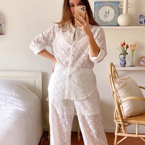 May include: White eyelet pajama set with a long-sleeved shirt and wide-leg pants. The shirt has a button-up front and a collar. The pants have a straight leg and a relaxed fit.