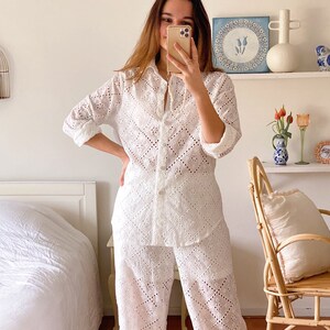 May include: A white, long-sleeved, button-up shirt and matching pants with a delicate eyelet pattern. The outfit is made of a lightweight fabric and has a relaxed fit.