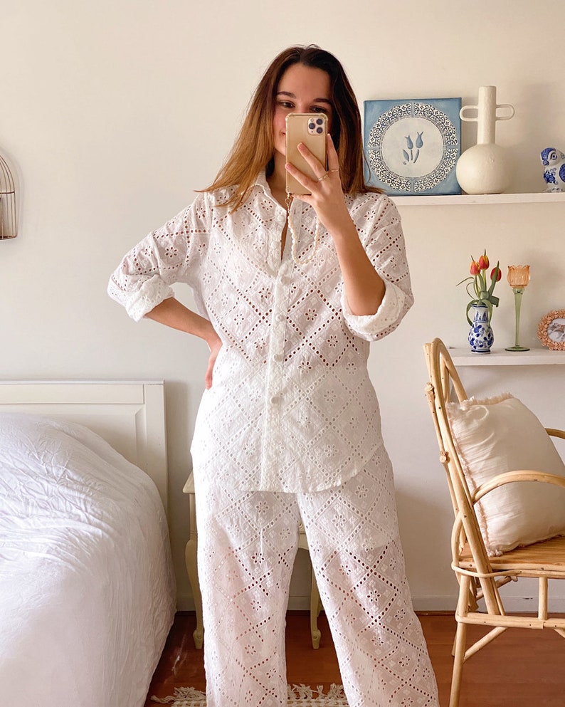 May include: A white, long-sleeved, button-up shirt and matching pants with a delicate eyelet pattern. The outfit is made of a lightweight fabric and has a relaxed fit.