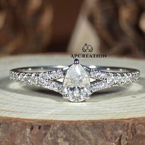 Peut inclure: Une bague de fiançailles en or blanc avec un diamant de forme poire, une monture à double bande et des diamants pavés.