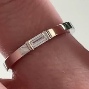 May include: A silver band ring with two small, rectangular, clear gemstones.