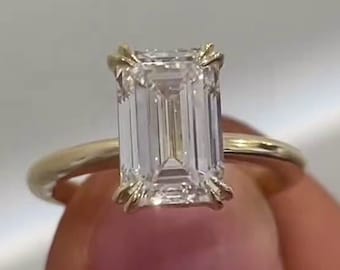 May include: A gold band engagement ring with a large, clear emerald cut diamond.