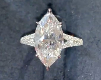 Może przedstawiać: Złoty pierścionek zaręczynowy z diamentem w szlifie markizy, z srebrną obrączką i mniejszymi diamentami osadzonymi na obrączce.