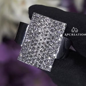 May include: A square-shaped ring with a silver band and a large, sparkly, black stone.