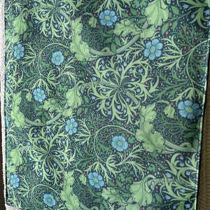 Op de afbeelding: Een decoratieve kussensloop met een bloemenpatroon. De sloop heeft een donkerblauwe achtergrond met een herhalend ontwerp van groene bladeren en lichtblauwe bloemen. Met een knoopsluiting.