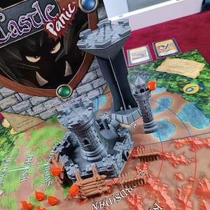 May include: Castle Panic board game with a game board, castle towers, and game pieces. The game board features a forest and a castle under attack. The box art shows the game's title and a monster.