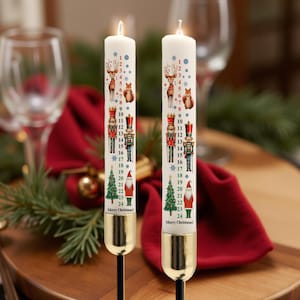 May include: Two lit white Advent candles, each decorated with festive illustrations of reindeer, squirrels, nutcrackers, Christmas trees, and Santa Claus. The candles are numbered 1-24, with "Merry Christmas!" at the base.