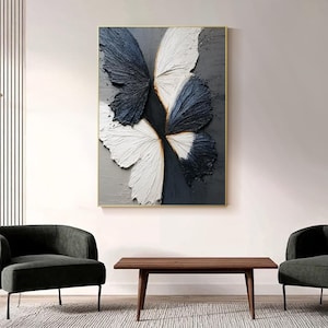 Pu&ograve; includere: Opera d'arte astratta a farfalla in cornice dorata. L'opera presenta ali strutturate nei toni del bianco e blu navy su sfondo grigio. Un elemento di arredo moderno per la casa, adatto a soggiorni o camere da letto.