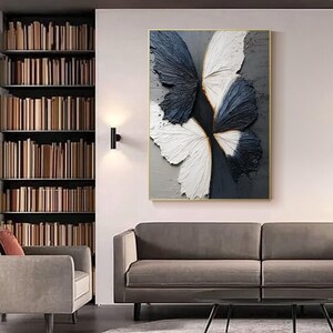 Pu&ograve; includere: Dipinto astratto incorniciato con un design a farfalla. Le ali sono raffigurate in blu navy e bianco strutturato, su uno sfondo grigio e grigio scuro. L'opera d'arte &egrave; esposta in un salotto.