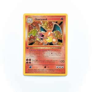May include: A Charizard Pokémon trading card. The card features a fiery orange Charizard illustration with blue wings. The card has text that reads "Charizard" and "120 HP". The card is a Stage 2 card.