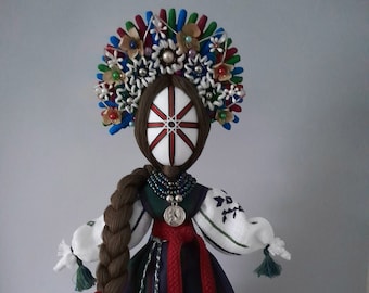 May include: A traditional folk doll with a white face, red and white striped head covering, and long brown braid. The doll is wearing a white blouse, a red sash, and a blue and green skirt. The doll is wearing a crown of flowers and beads.