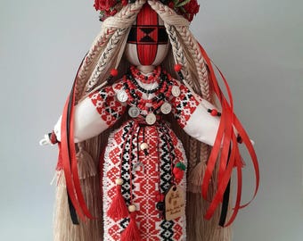 May include: A handcrafted fabric doll featuring long blonde braided hair adorned with a crown of red roses. The doll wears a white dress with intricate red and black geometric embroidery, layered necklaces with silver coins, and red ribbons.