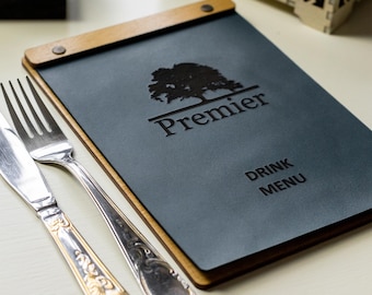 Puede incluir: Un menú de cuero azul oscuro con un marco de madera. El menú tiene un logotipo de un árbol con la palabra "Premier" debajo. El texto "Drink Menu" está impreso debajo del logotipo.
