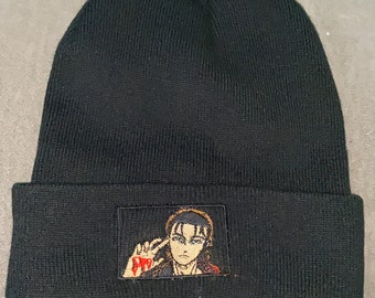 May include: Black beanie with a small embroidered patch of an anime character with red eyes and brown hair. The character is making a hand gesture with their right hand.