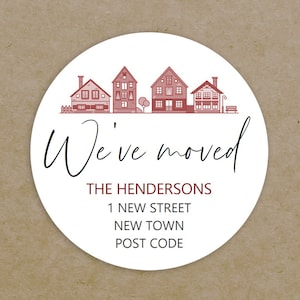 May include: A white circle sticker with a red and white illustration of a row of houses. The text "We've moved" is written in black cursive script. Below the houses, the text "THE HENDERSONS", "1 NEW STREET", "NEW TOWN", and "POST CODE" is written in red.
