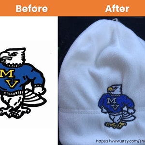 May include: White fleece beanie with an embroidered blue and yellow eagle wearing a blue sweater with the letters "MV" on it.