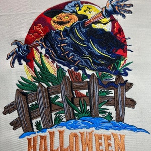 May include: Embroidered Halloween design. A scarecrow with a jack-o'-lantern head, wearing a dark cloak, and reaching out. A wooden fence and the word "HALLOWEEN" are below. The background includes a full moon and red clouds.