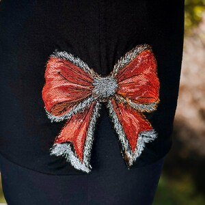 May include: A black fabric hat with a large red and silver embroidered bow on the back.
