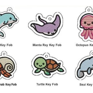 May include: A collection of embroidered key fobs featuring marine life. Designs include a dolphin, manta ray, octopus, hermit crab, turtle, and seal. Each fob has a white outline and the name of the animal below it.