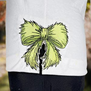 May include: A white shirt with a green embroidered bow on the back.