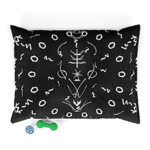 May include: Black pet bed featuring a white abstract pattern. The bed has a rectangular shape and a soft, plush texture. A blue and green dog toy is in front of the bed.