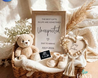 May include: A wicker basket holds a teddy bear, ultrasound image, and baby booties. A framed sign reads "THE BEST GIFTS IN LIFE ARE SOMETIMES Unexpected DUE TO ARRIVE JULY 2026." A heart-shaped decoration with "Baby Jonathan" hangs nearby. Dried flowers add a decorative touch.