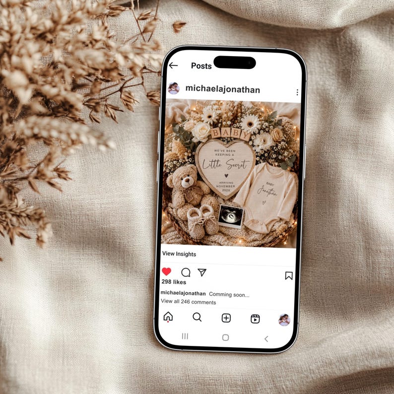 May include: A smartphone displaying an Instagram post by michaelajonathan featuring a pregnancy announcement. The image shows a heart-shaped sign reading We've been keeping a little secret, a teddy bear, baby booties, a onesie, and an ultrasound.