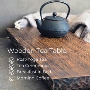 May include: A black cast iron teapot rests on a rectangular wooden tea table. The table has a natural wood grain and a dark finish. Text on the table reads "Wooden Tea Table" with checkmarks for "Post-Yoga Tea", "Tea Ceremonies", "Breakfast in Bed", and "Morning Coffee".