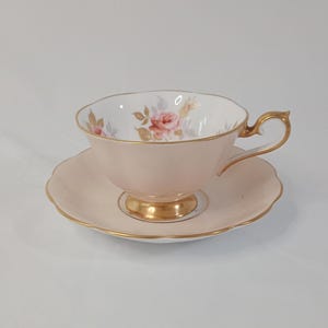 May include: A pink teacup and saucer with a floral design and gold trim. The cup has a delicate handle and the saucer has a scalloped edge.