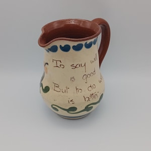 以下が含まれることがあります： 茶色の縁と取っ手を持つ、クリーム色の小さな陶器のピッチャー。青と緑の花柄と「To say well is good but to do well is better.」という引用が書かれています