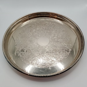 May include: A silver serving tray with a decorative embossed design. The tray is round and has a raised rim.