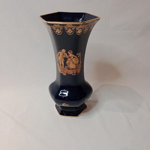 May include: A dark blue ceramic vase with gold accents and a gold-painted scene of a couple dancing. The vase has a hexagonal shape and a narrow neck.