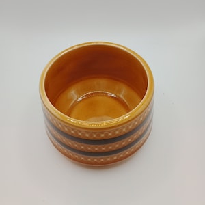 May include: A small, round, orange ceramic planter with a brown and white geometric pattern around the rim.