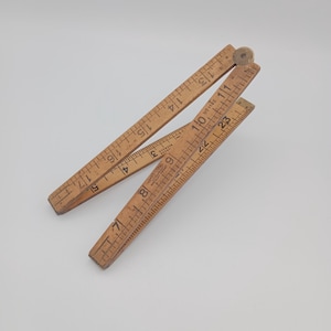 May include: A wooden folding ruler with markings from 1 to 23 inches. The ruler is made of light brown wood and has a worn, vintage look.