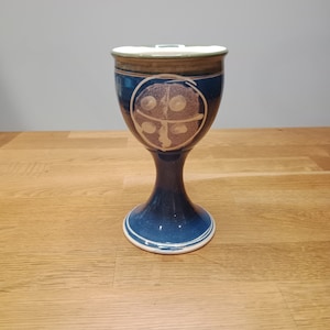 Può includere: Un calice in ceramica blu con un disegno bianco sul davanti. Il calice ha un bordo verde e una base bianca.