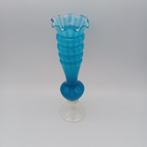 May include: A blue glass vase with a ruffled top and a clear glass base. The vase has a textured, rippled design.
