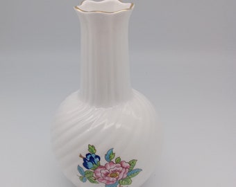 Puede incluir: Jarrón de cerámica blanca con base bulbosa y cuello acanalado. El jarrón presenta un diseño floral con detalles en rosa, azul y verde. El borde está adornado con oro. Una pieza decorativa para exhibir flores o como acento.