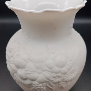 May include: White ceramic vase with an embossed floral design. The vase has a scalloped rim and a round body.