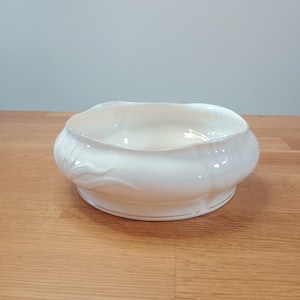 Può includere: Una ciotola in ceramica bianca con un bordo dorato. La ciotola ha un design a coste ed è perfetta per servire spuntini o dessert.