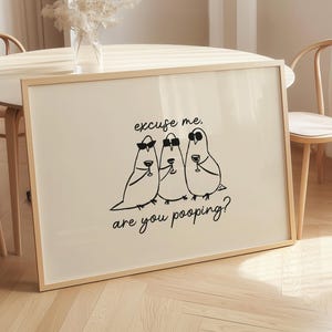 May include: A framed art print featuring three cartoon birds in sunglasses, each holding a wine glass. The black text reads "excuse me, are you pooping?" The artwork is displayed on a light-colored background.