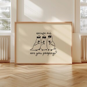 May include: A framed print featuring three cartoon birds wearing sunglasses and holding wine glasses. The text on the print reads "excuse me, are you pooping?" The artwork is displayed on a light-colored background.