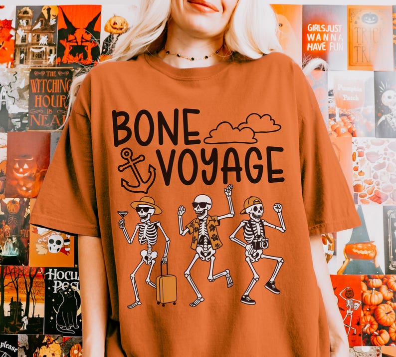 May include: An orange t-shirt with the words "BONE VOYAGE" and an anchor graphic. Below the text are three skeleton figures, one holding a cocktail, one with a suitcase, and one with a camera. The shirt has a crew neck and short sleeves.