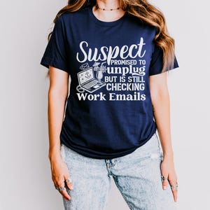 May include: A navy blue t-shirt with a white graphic that says "Suspect Promised to Unplug But is Still Checking Work Emails". The graphic includes a laptop, a cocktail, and an anchor.