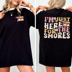 Op de afbeelding: Zwart T-shirt met een afbeelding van een s'more op de voorkant en de tekst "I'm just here for the smores" op de achterkant.