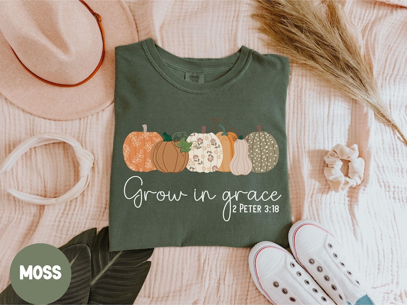 May include: A green t-shirt with a row of five pumpkins with floral patterns. The text "Grow in grace 2 Peter 3:18" is printed below the pumpkins.