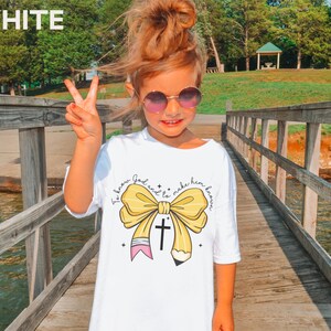 May include: White t-shirt with a yellow bow and a pencil with a cross on it. The text on the shirt says "To know God and to make him known."