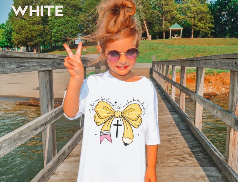 May include: White t-shirt with a yellow bow and a pencil with a cross on it. The text on the shirt says "To know God and to make him known."